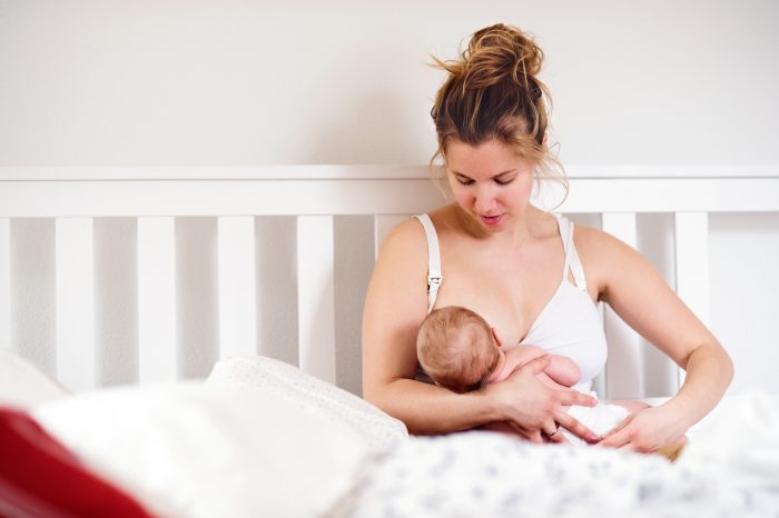 Young mother breastfeeding her cute newborn baby son, home bedroom