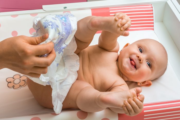 Mother changing diaper to her little baby girl in child room at home