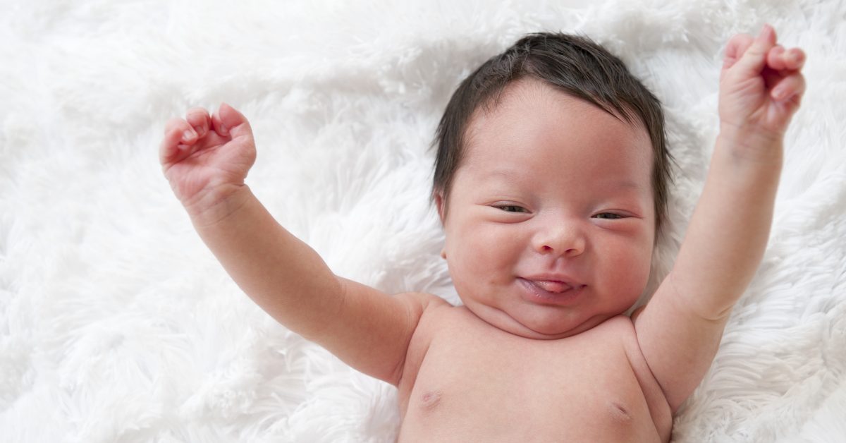 Happy newborn baby with arms up in the air.